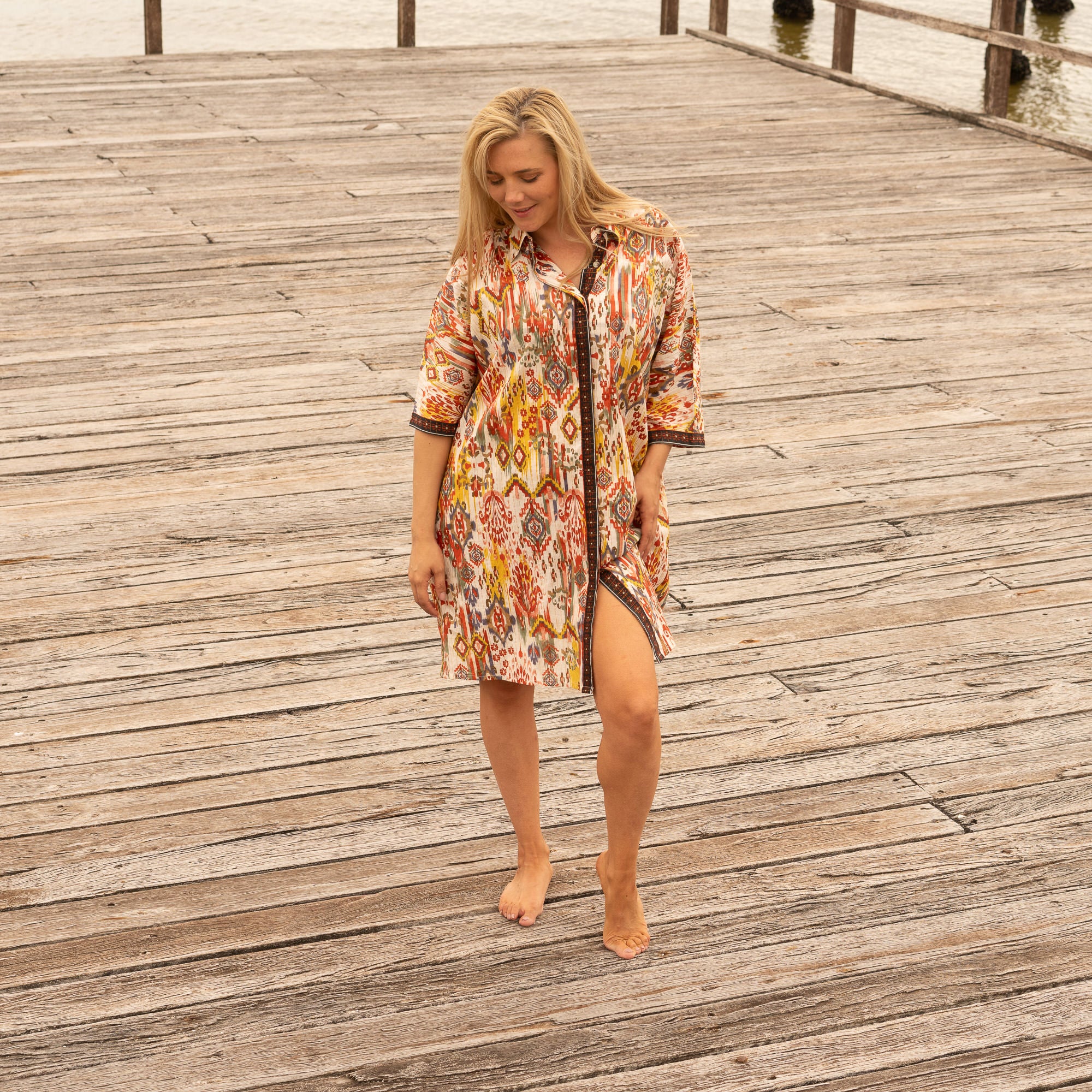 Woman wearing a patterned dress on a wooden dock by water