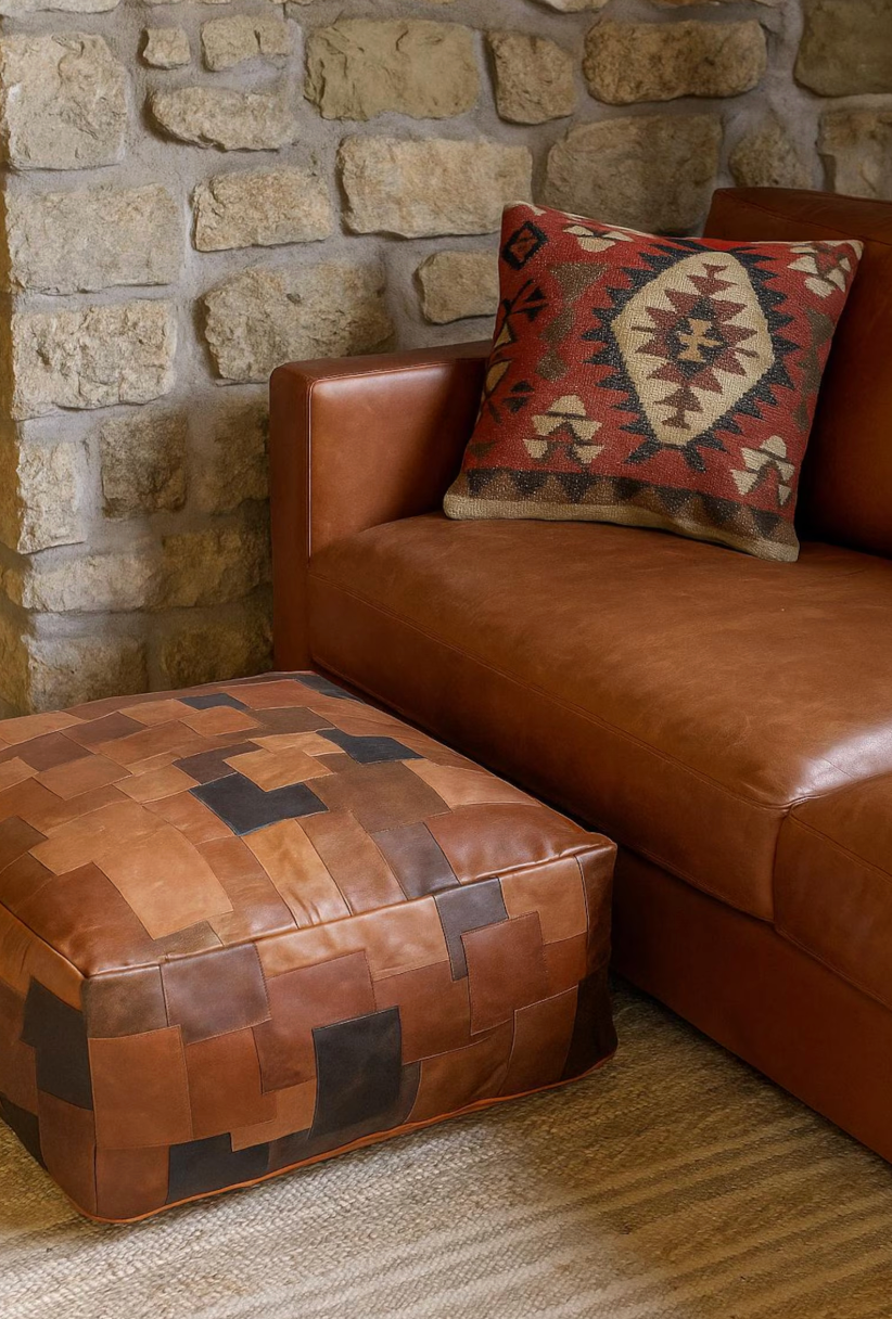 Square leather patchwork floor ottoman in tan brown tones placed on a rug in a neutral lounge room