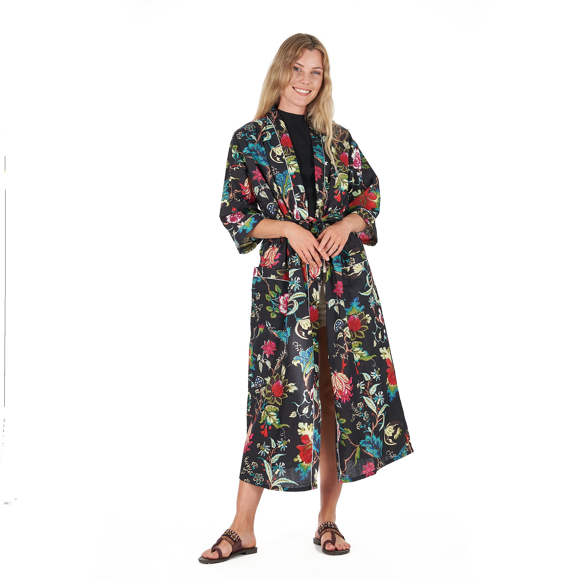 A woman standing and smiling, wearing a multicolored floral kimono robe with three-quarter sleeves and a matching tie belt.
