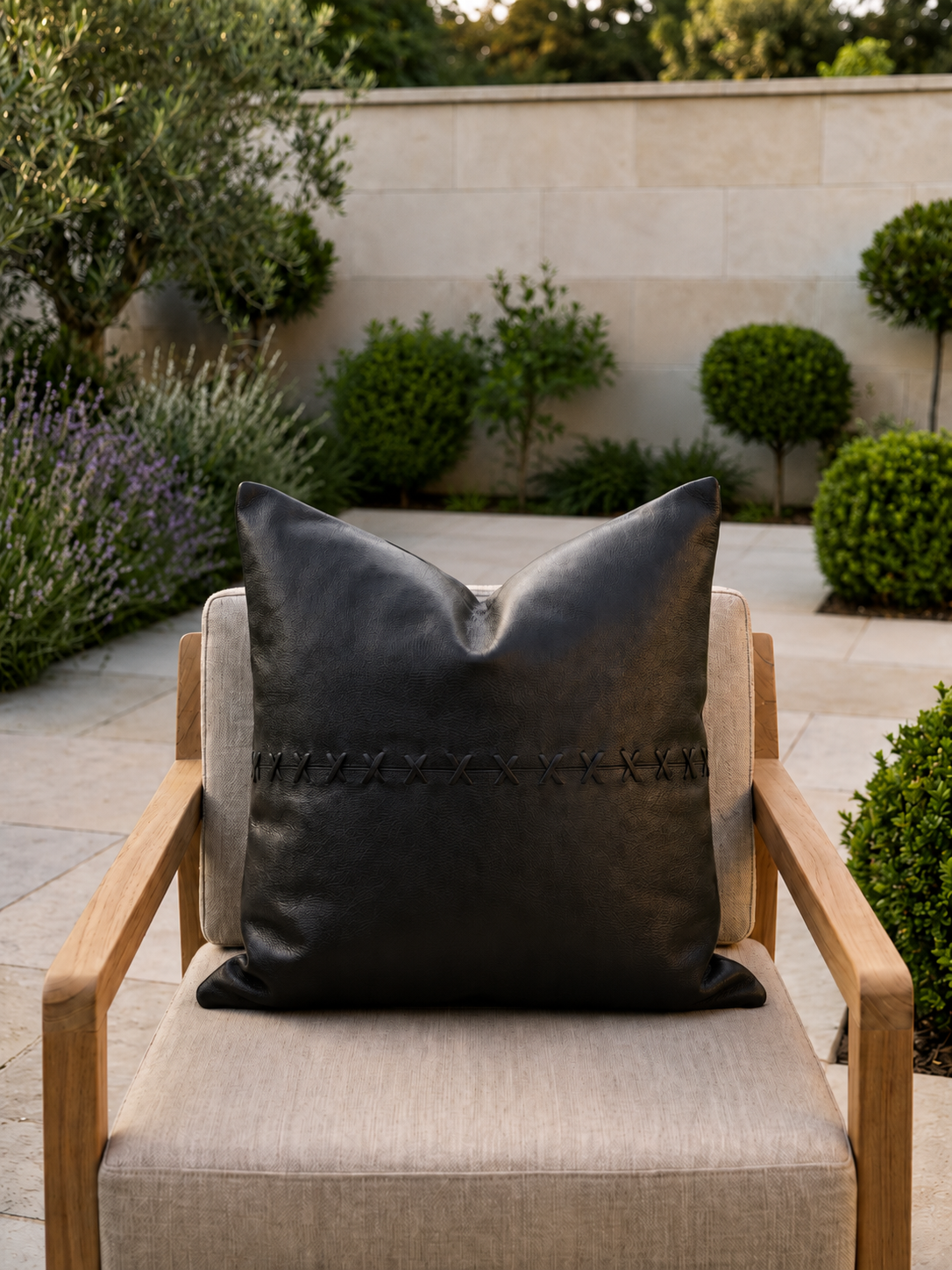 Gray pillow on a chair in an outdoor setting with plants and a wall in the background
